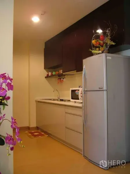 Condominium for rent or sale in Watthana, Bangkok - Compact kitchenette with upper dark cabinets, sink, microwave and a tall silver refrigerator in a Sukhumvit-area condominium.