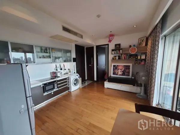 Condominium for rent in Yan Nawa, Bangkok - Living and kitchen area with TV wall, shelving and sliding doors to the balcony.