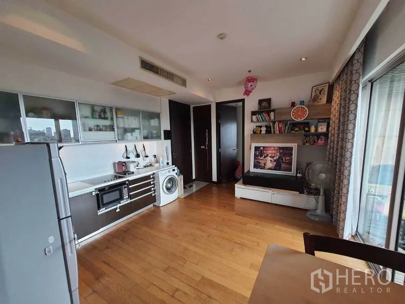 Condominium for rent in Yan Nawa, Bangkok - Living and kitchen area with TV wall, shelving and sliding doors to the balcony.