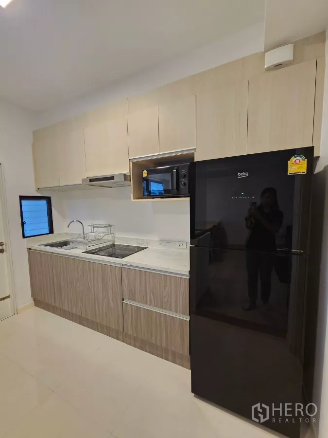 Townhouse for rent in Bang Phli, Samut Prakan - Full kitchen with black refrigerator, microwave, hob and light wood cabinetry