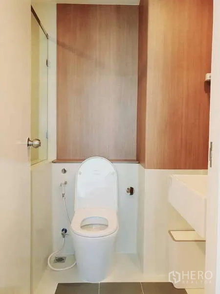 Condominium for rent in Sathon, Bangkok - Second bathroom with toilet and wood accent wall beside the shower.