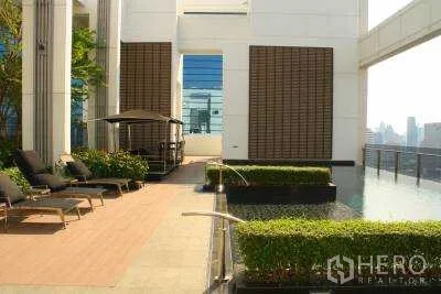 Condominium for rent in Huai Khwang, Bangkok - Rooftop garden deck with sun loungers, trimmed hedges, and a reflecting water feature overlooking the city.