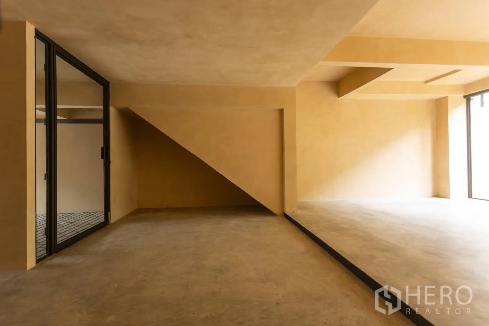 Home Office for rent in Watthana, Bangkok - Under‑stair alcove and split‑level concrete workspace with natural light.