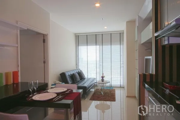 Condominium for rent in Khlong Toei, Bangkok - Bright living and dining area with breakfast bar, leather sofa, and floor‑to‑ceiling windows leading to a balcony.