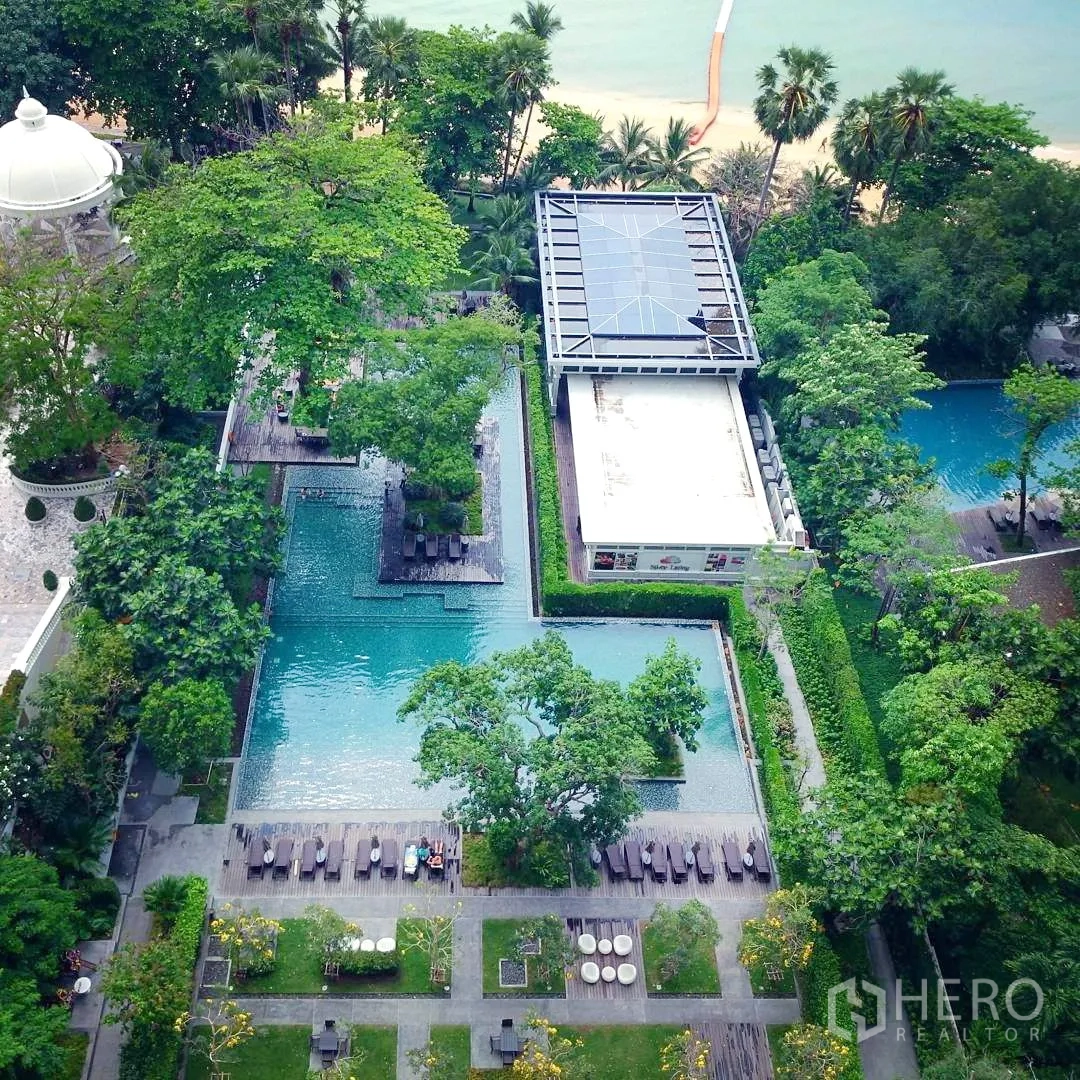 Condominium for rent or sale in Bang Lamung, Chon Buri - Aerial view of resort-style swimming pools and landscaped tropical gardens by the beach.