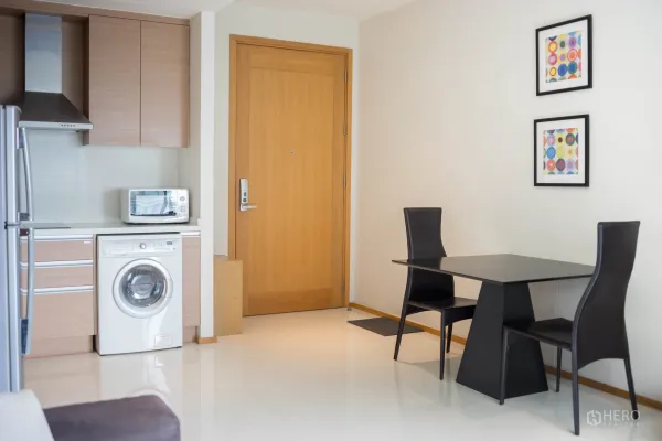 Condominium for rent or sale in Khlong Toei, Bangkok - Open-plan kitchenette with appliances, washing machine and a two-seat dining table.