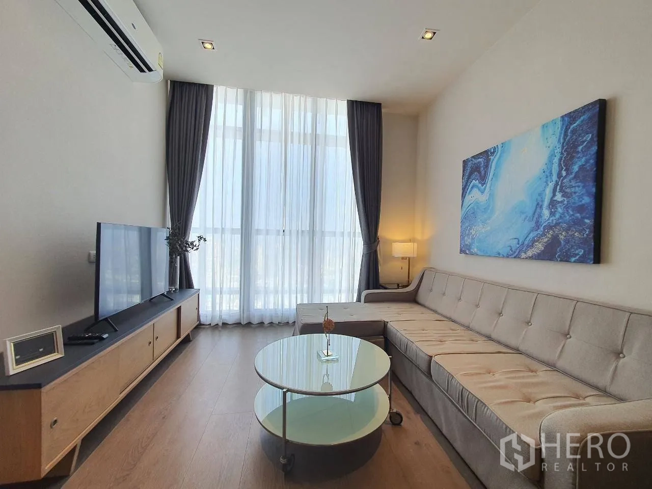 คอนโด for rent in Khlong Toei, Bangkok - ห้องนั่งเล่นพร้อมชั้นวางทีวี งานศิลป์ และหน้าต่างสูงโปร่งพร้อมผ้าม่านบาง
