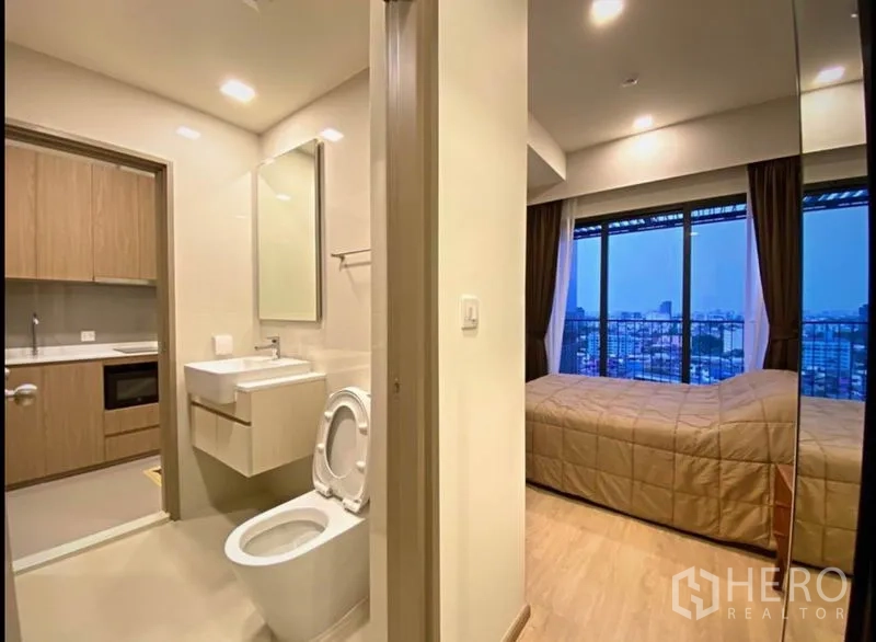 Condominium for sale in Huai Khwang, Bangkok - Hallway view to a modern bathroom and a bedroom with floor-to-ceiling windows and city skyline.