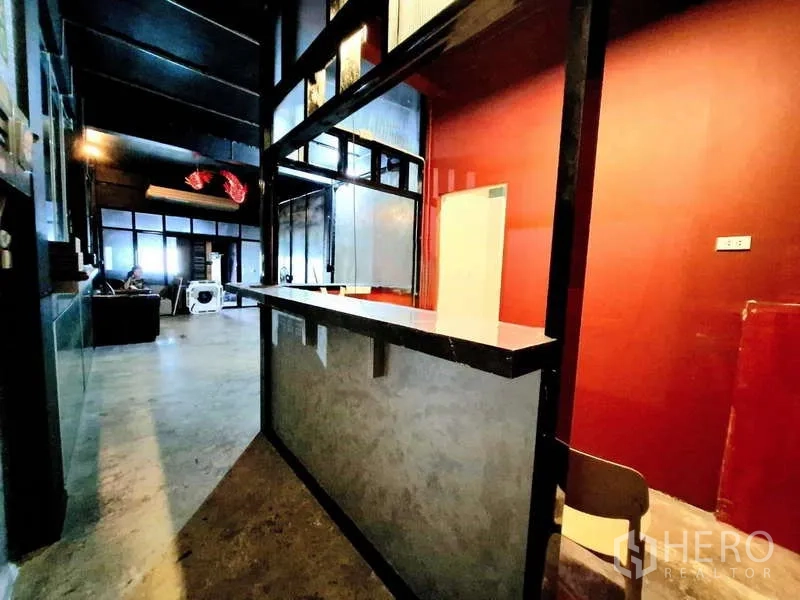 店屋 出租在Bang Rak, Bangkok - 红色背景墙与长形水泥吧台，黑色金属框架。
