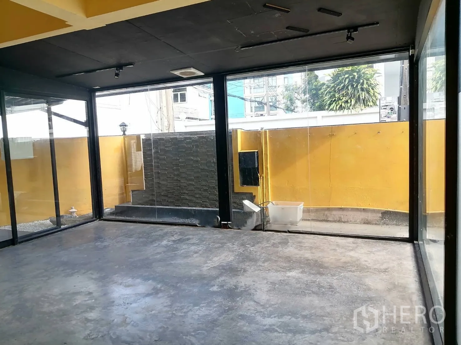 Detached House for rent in Watthana, Bangkok - Bright room enclosed by tall glass walls overlooking a small courtyard and yellow boundary wall.