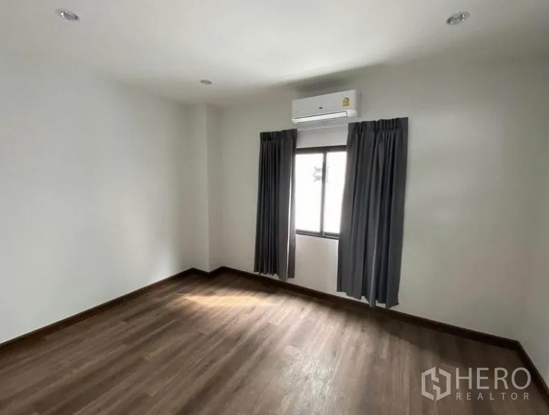 联排别墅 出租在Bang Na, Bangkok - 带空调的卧室，木地板、白色墙面与窗帘窗