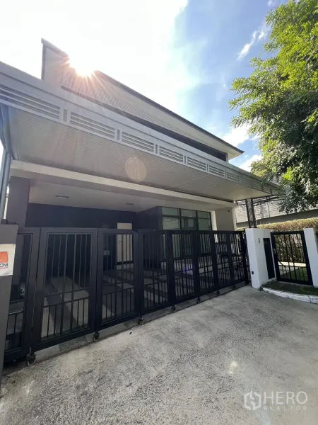 独立式住宅 出售在Bang Kapi, Bangkok - 现代两层转角别墅，黑色推拉大门，阳光洒落。