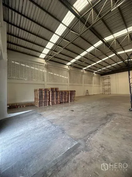 货栈 出租在Suan Luang, Bangkok - 仓库内有堆放的木托盘，光滑混凝土地面与通透金属屋顶。