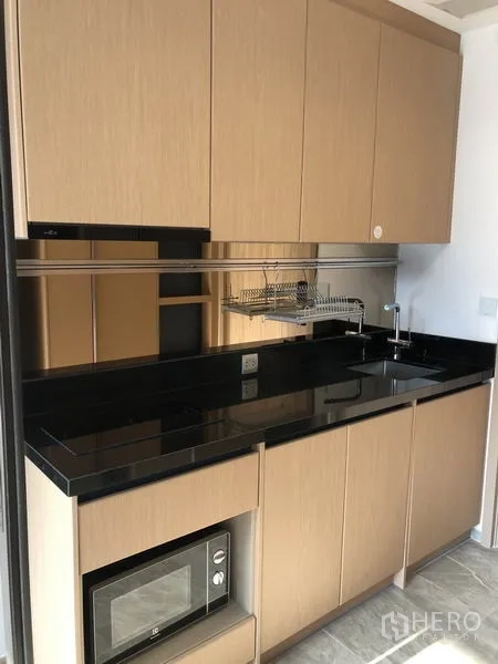 คอนโด ให้เช่าในWatthana, Bangkok - ครัวขนาดกะทัดรัด เคาน์เตอร์หินสีดำ อ่างล้างมือ เตา เครื่องไมโครเวฟ และตู้เก็บของ