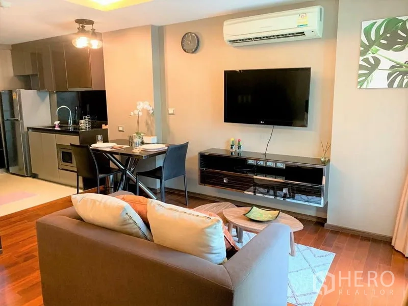 Condominium for rent in Watthana, Bangkok - Living area with wall-mounted TV, air conditioner, dining table and sleek kitchen cabinetry.