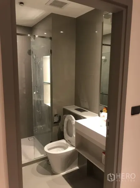 公寓 出租在Phra Khanong, Bangkok - 现代化浴室，玻璃淋浴房、洗手台与马桶，配色简洁。