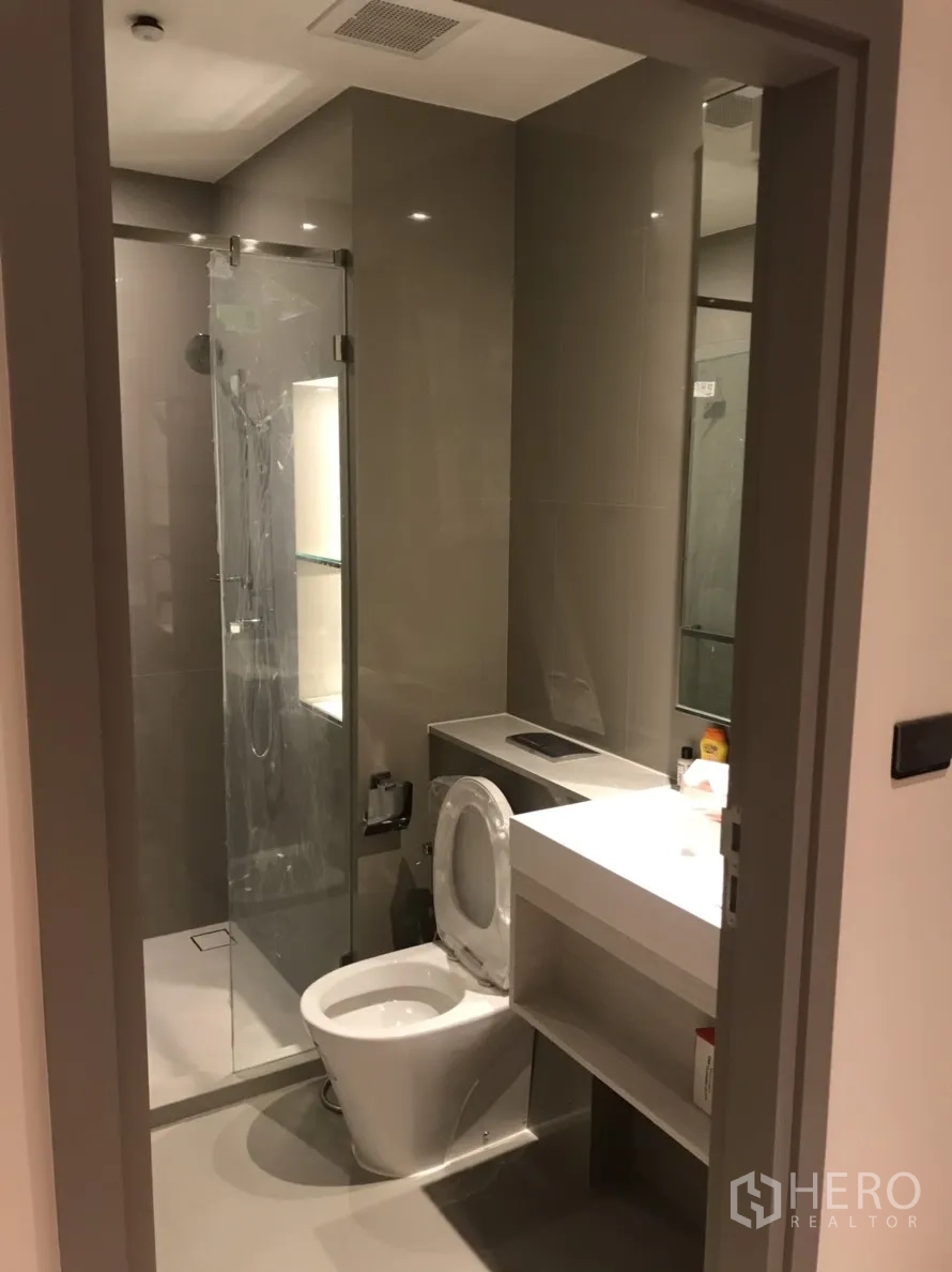 公寓 出租在Phra Khanong, Bangkok - 现代化浴室，玻璃淋浴房、洗手台与马桶，配色简洁。
