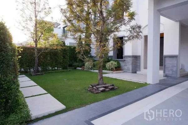 Detached House for rent in Saphan Sung, Bangkok - Landscaped front garden with trees, hedge boundary, stepping-stone path and modern house exterior.