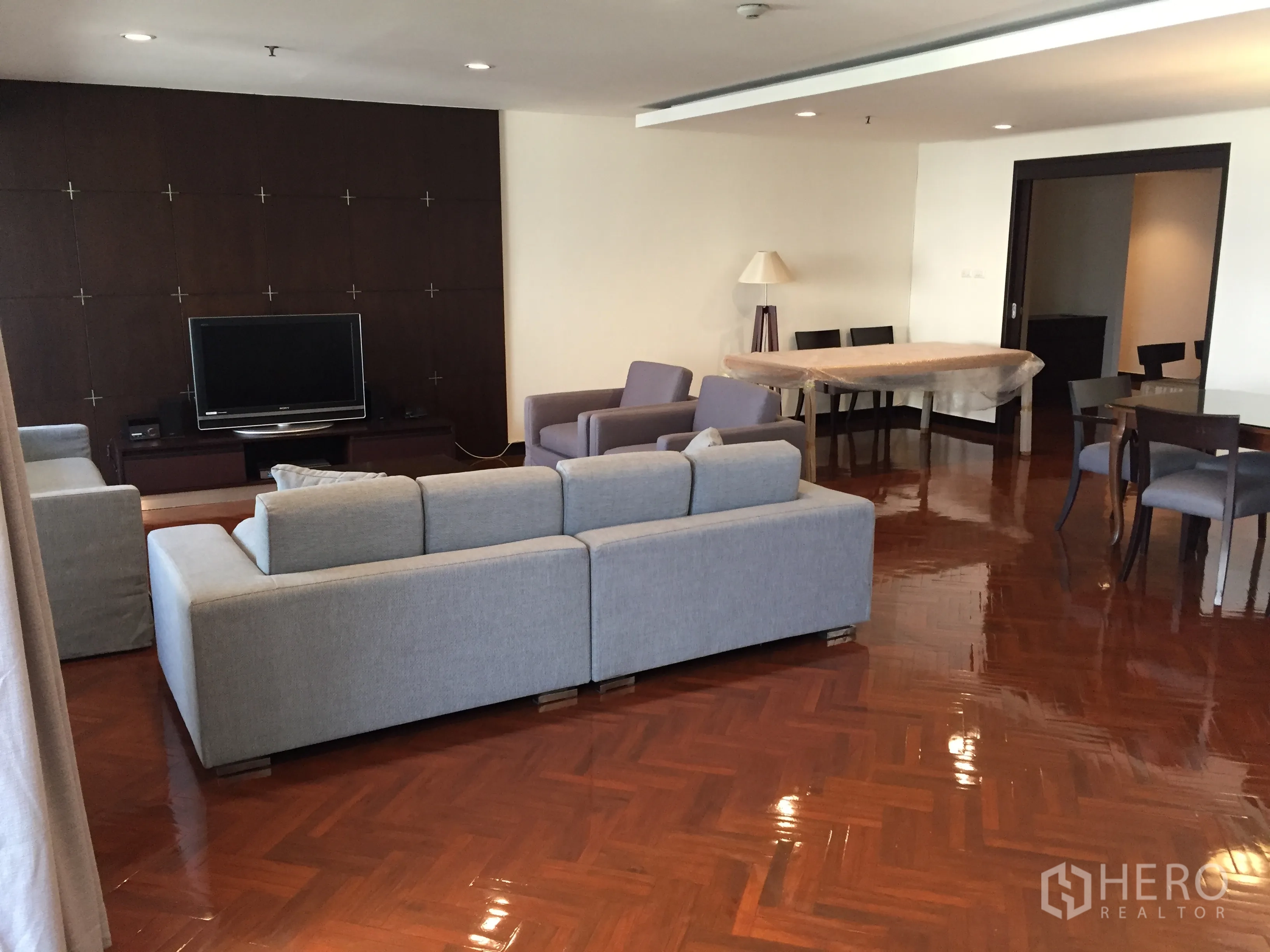Condominium for rent in Watthana, Bangkok - Open-plan living and dining area with grey sofas and TV feature wall.