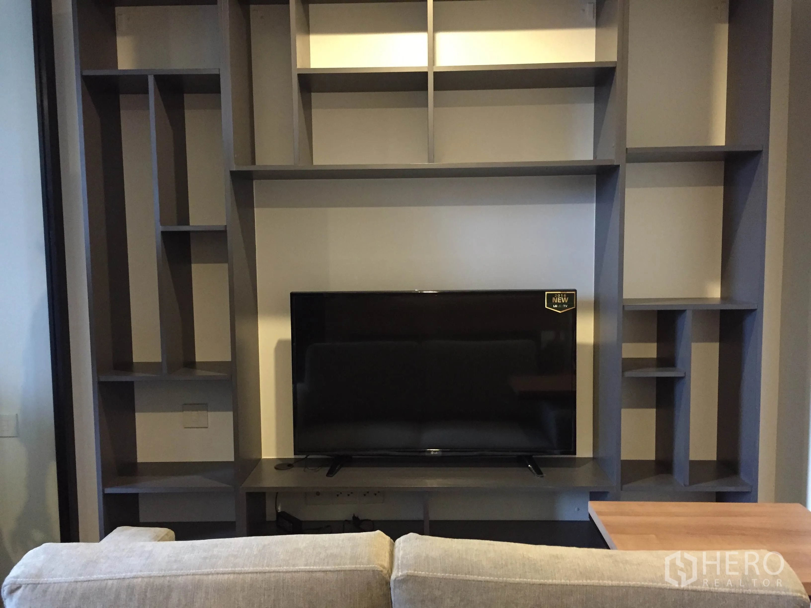 Condominium for rent in Pathum Wan, Bangkok - Living room with built-in grey shelving, flat-screen TV and a sofa.