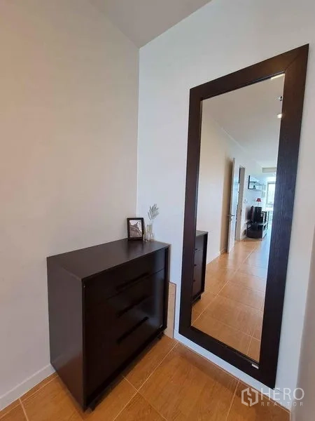 Condominium for rent in Khlong Luang, Pathum Thani - Entry corner with tall frameless mirror and dark wood chest of drawers.