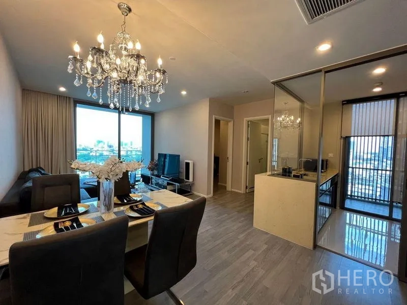 คอนโด ให้เช่าในWatthana, Bangkok - ห้องนั่งเล่นและทานข้าวแบบเปิดโล่ง โคมระย้า โซฟา ทีวี และครัวปิดผนังกระจก มองเห็นวิวเมือง