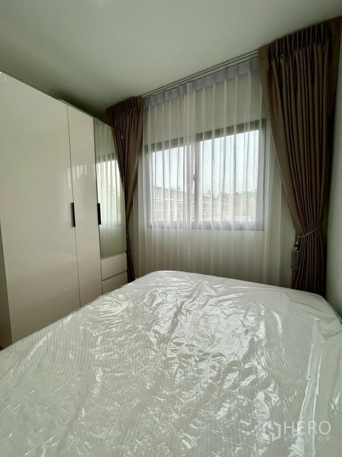 Townhouse for rent in Bang Phli, Samut Prakan - Bedroom with bed wrapped in plastic and wardrobe by window.