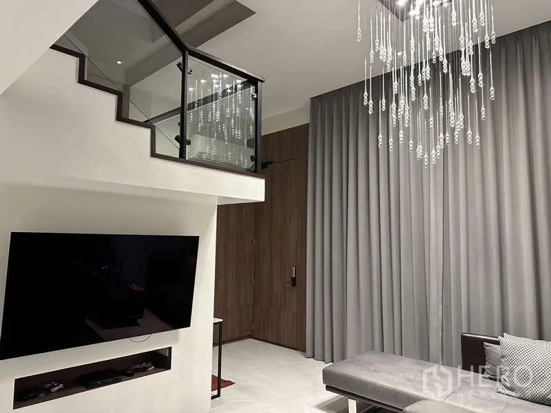 Townhouse for rent in Yan Nawa, Bangkok - Living room with floating staircase, glass balustrade, TV wall and chandelier.