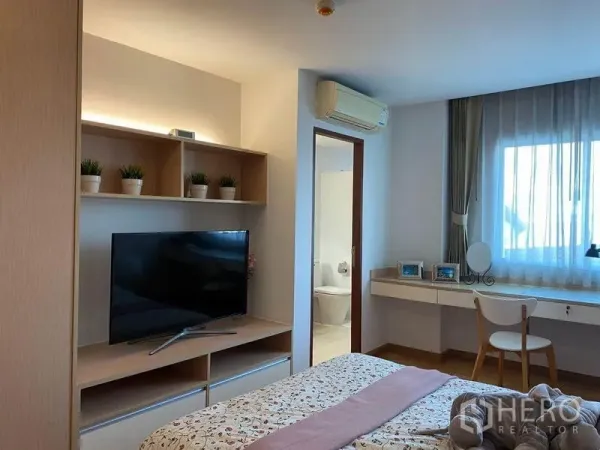 公寓 出租或出售在Phra Khanong, Bangkok - 帕卡隆公寓主卧，带电视柜与开放置物架，窗边书桌，并有通往卫浴的门。