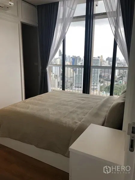 Condominium for rent in Khlong Toei, Bangkok - Bright bedroom with queen bed and panoramic city view through tall windows.
