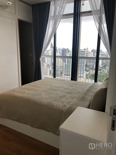 Condominium for rent in Khlong Toei, Bangkok - Bright bedroom with queen bed and panoramic city view through tall windows.