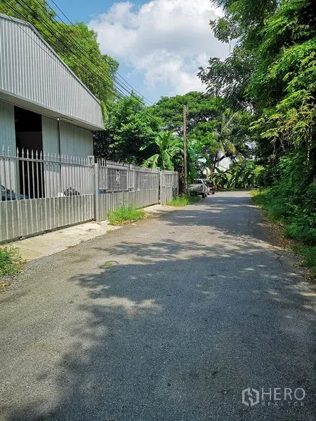 货栈 出租在Bang Khen, Bangkok - 仓库围栏旁的绿荫通道，适合卡车进出与装卸。