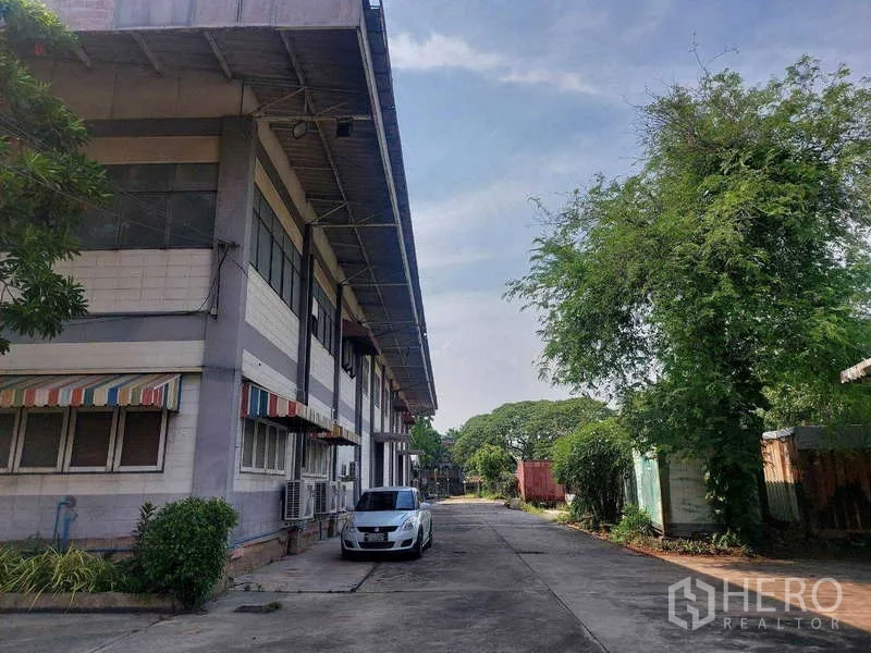 Warehouse for rent in Min Buri, Bangkok - Warehouse exterior with driveway, parking space and mature greenery.