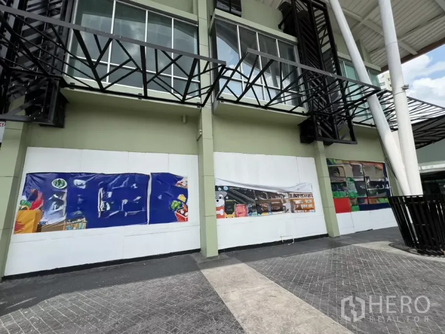 พื้นที่ขายปลีก ให้เช่า - ด้านหน้าร้านชั้นถนน มีป้ายชั่วคราวกว้าง ใต้กันสาดโลหะและกระจกชั้นบน