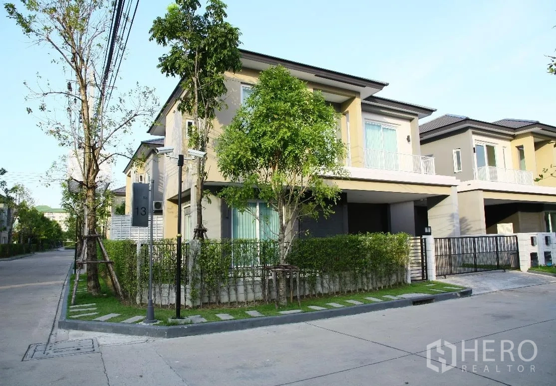 Detached House for rent or sale in Bang Na, Bangkok - Corner view of a modern two-storey detached house with gated fence and trees on a quiet street in Bang Na.