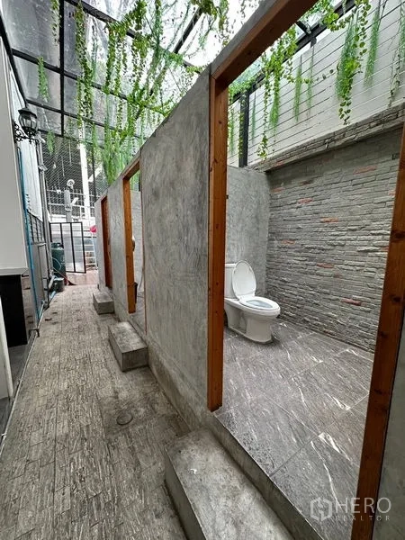 Retail Space for rent in Suan Luang, Bangkok - Restroom area with open-top stalls, stone-textured walls and overhead greenery beneath a clear roof.