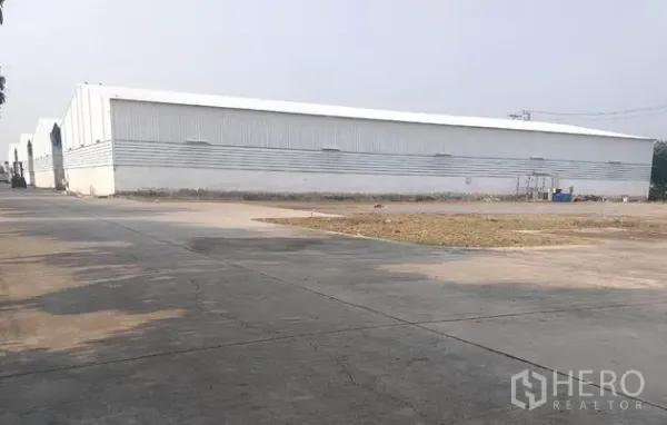 Warehouse for rent in Pathum Thani - Exterior of a metal-clad warehouse with a wide concrete yard and driveway.