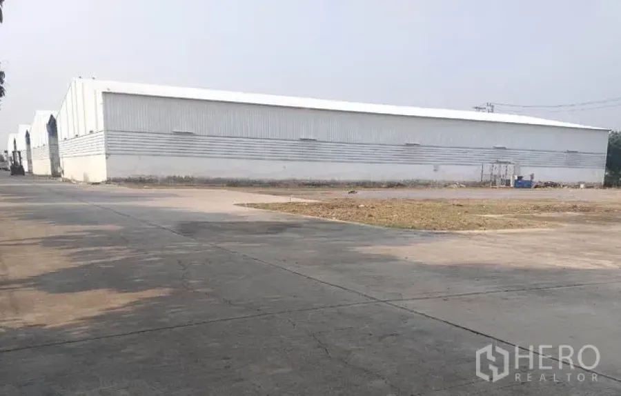 Warehouse for rent in Pathum Thani - Exterior of a metal-clad warehouse with a wide concrete yard and driveway.