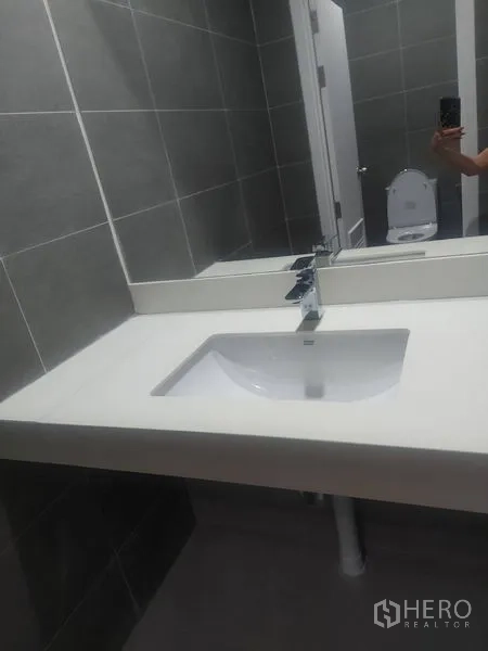 零售空间 出租 - 现代化卫生间，灰色瓷砖墙，宽台面洗手盆与大镜子。