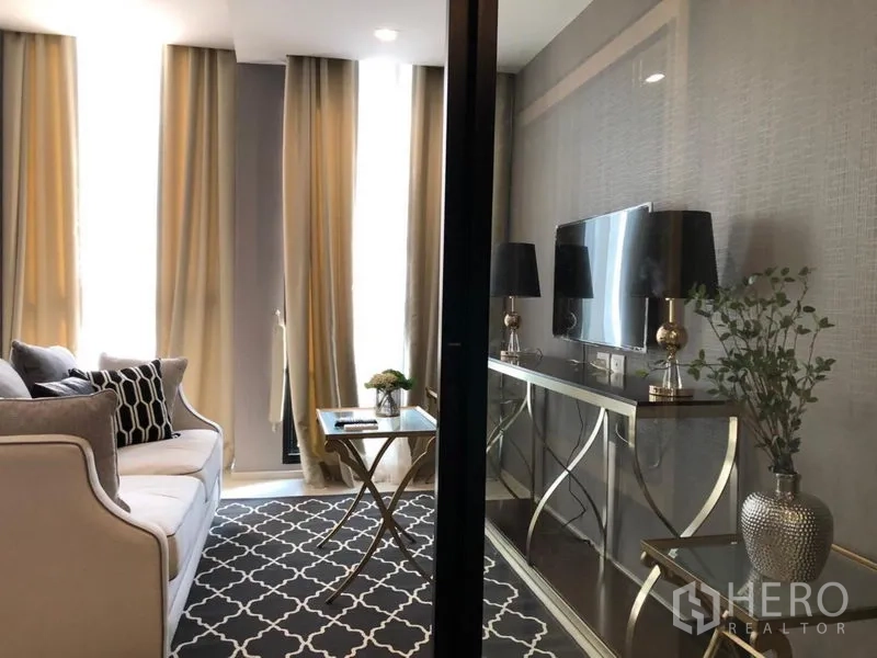 Condominium for rent in Pathum Wan, Bangkok - Compact lounge with patterned rug, sofa, TV and floor-to-ceiling windows.