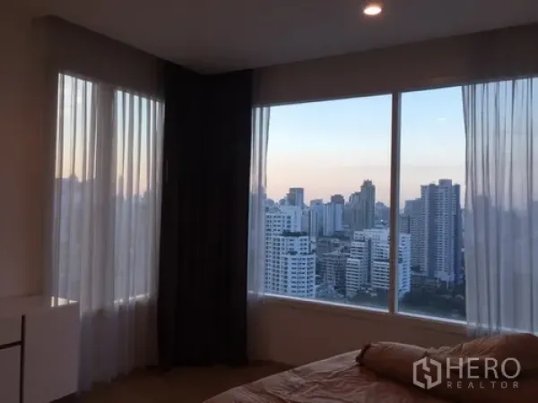 Condominium for rent in Watthana, Bangkok - Corner bedroom with large windows and panoramic Bangkok city view at sunset.