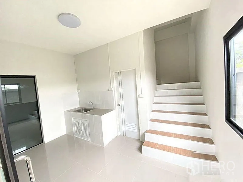 工厂 出租在Bang Bua Thong, Nonthaburi - 一层厨房区，不锈钢水槽、玻璃门及通往二层的楼梯。