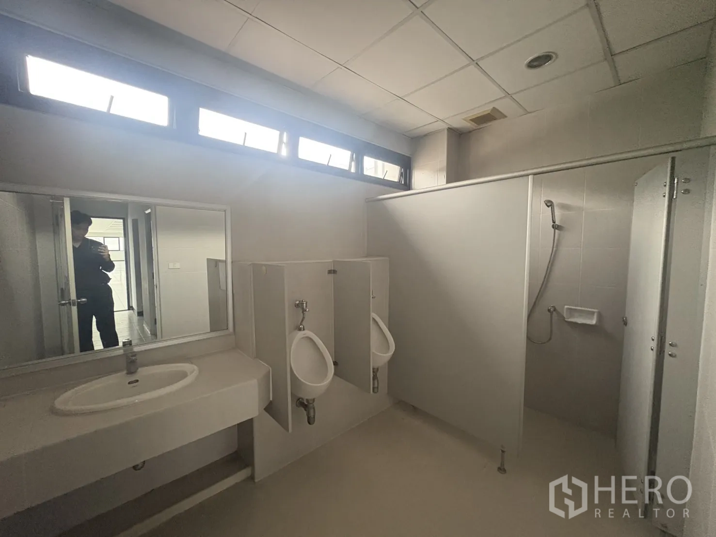 Factory for rent or sale in Samut Prakan - Street view of the fenced factory complex with wide road and parked car.