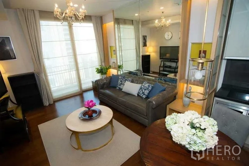Condominium for rent in Watthana, Bangkok - Cozy lounge with mirrored feature wall, chandelier, round table and tall curtains by balcony doors.