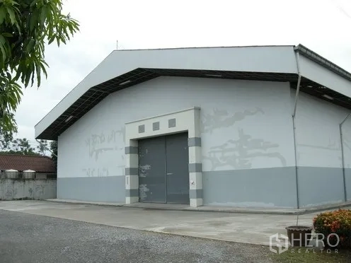 Warehouse for rent in Nakhon Pathom - Clean warehouse exterior with wide metal entrance door and paved driveway in Nakhon Pathom.