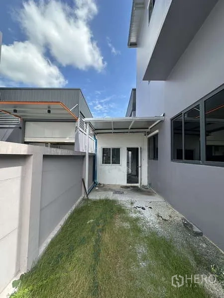 Factory for rent in Lam Luk Ka, Pathum Thani - Narrow side yard with a grass strip and a small covered rear entrance.