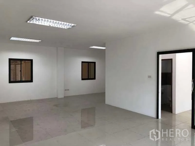 Factory for rent or sale in Bang Phli, Samut Prakan - Open office workspace with windows, fluorescent lighting and doorway access to a restroom.