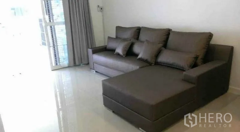 Townhouse for rent in Bang Phli, Samut Prakan - Bright living room with L-shaped gray sofa on glossy tiled floor near sliding door.