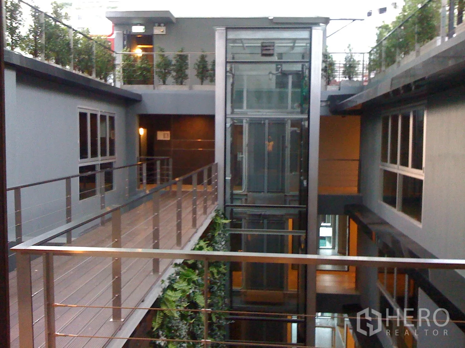 Condominium for rent or sale in Bang Rak, Bangkok - Contemporary building atrium with a glass elevator and skybridge corridors lined with greenery.