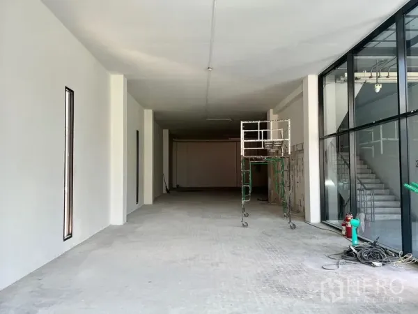 零售空间 出租 - 纵深商铺，整面玻璃临街、挑高天花，旁有脚手架与楼梯及消防设施。